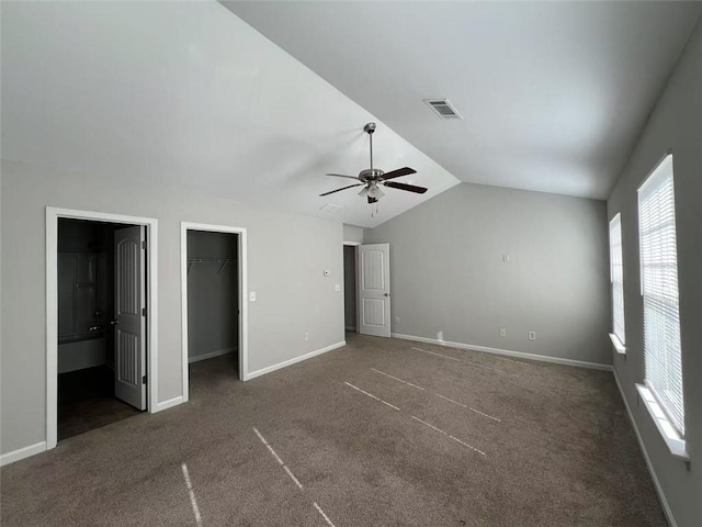 unfurnished bedroom featuring carpet, visible vents, a spacious closet, vaulted ceiling, and baseboards