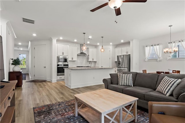 living room with a ceiling fan, a chandelier, light wood-style floors, and recessed lighting