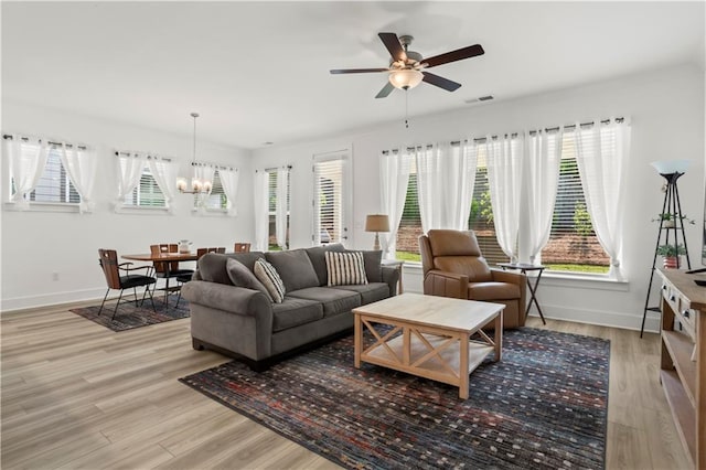 living area with a chandelier, light wood-style flooring, baseboards, and a ceiling fan