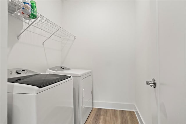 clothes washing area featuring washer and dryer, light wood-style flooring, and baseboards