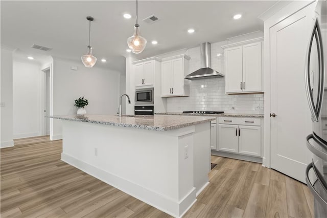 kitchen featuring wall chimney range hood, appliances with stainless steel finishes, decorative backsplash, light wood-type flooring, and white cabinets