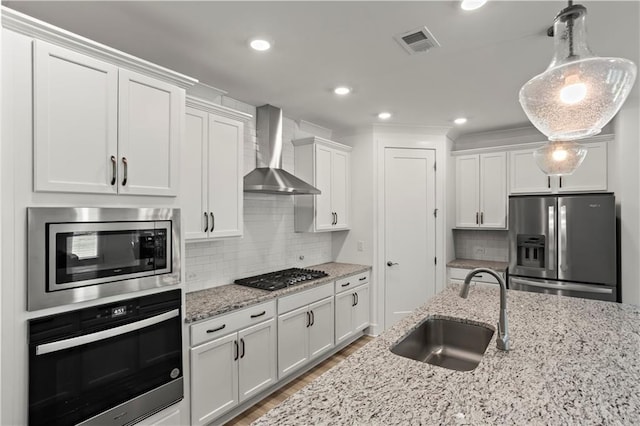 kitchen with stainless steel appliances, a sink, wall chimney range hood, white cabinetry, and backsplash