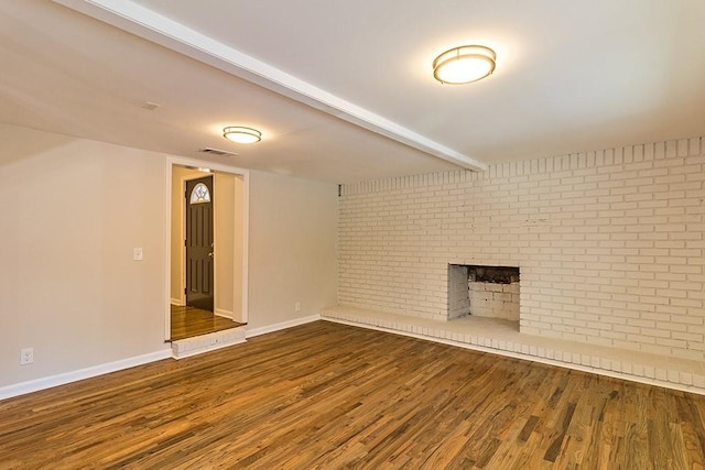 unfurnished living room with a brick fireplace, brick wall, hardwood / wood-style flooring, and beamed ceiling