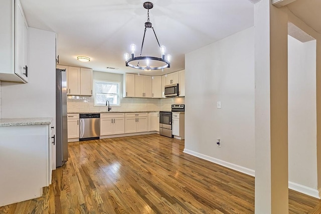 kitchen featuring decorative light fixtures, tasteful backsplash, white cabinetry, light wood-type flooring, and appliances with stainless steel finishes