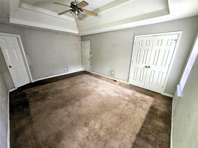 unfurnished bedroom featuring ceiling fan, a tray ceiling, and dark carpet