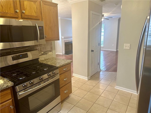 kitchen featuring crown molding, appliances with stainless steel finishes, light stone countertops, decorative backsplash, and light hardwood / wood-style floors