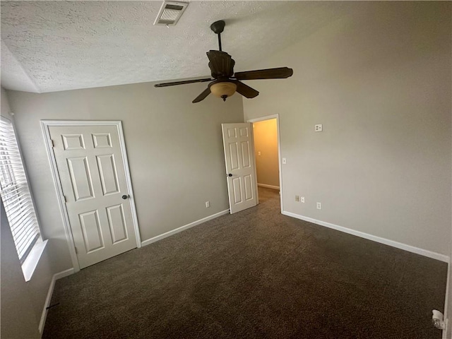 unfurnished bedroom featuring ceiling fan, multiple windows, a textured ceiling, and dark colored carpet