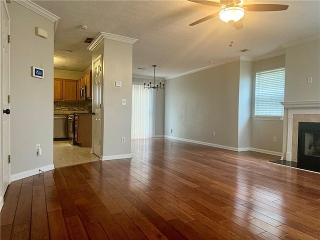 unfurnished living room with a fireplace, light wood-type flooring, ceiling fan with notable chandelier, and crown molding