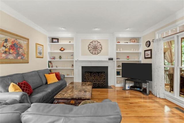 living area with light wood-style floors, ornamental molding, built in features, and a fireplace with flush hearth