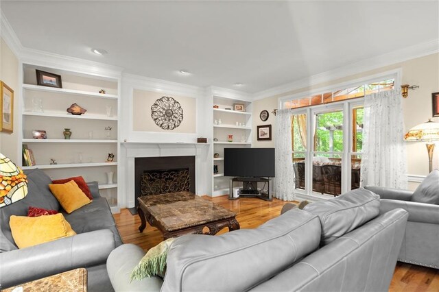 living area with built in features, ornamental molding, wood finished floors, and a fireplace