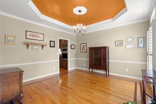 dining area with an inviting chandelier, ornamental molding, baseboards, a tray ceiling, and light wood finished floors
