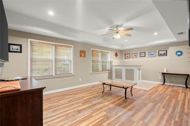interior space featuring a ceiling fan, baseboards, a raised ceiling, and light wood-type flooring