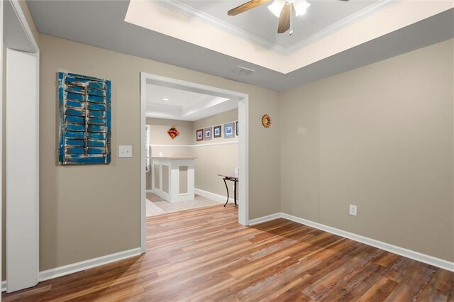 unfurnished room featuring crown molding, wood finished floors, baseboards, a raised ceiling, and a ceiling fan