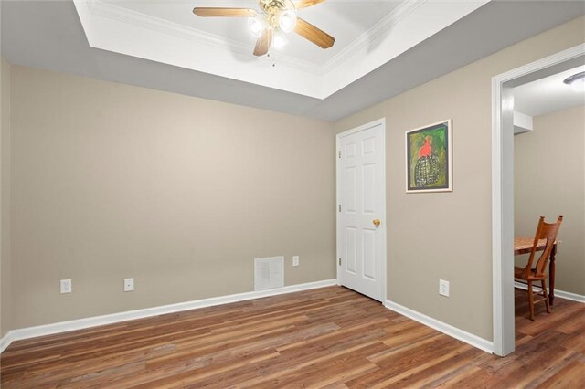 unfurnished room with ceiling fan, visible vents, wood finished floors, a raised ceiling, and baseboards