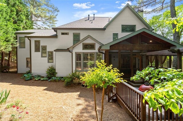 rear view of property featuring a shingled roof, a sunroom, and a chimney