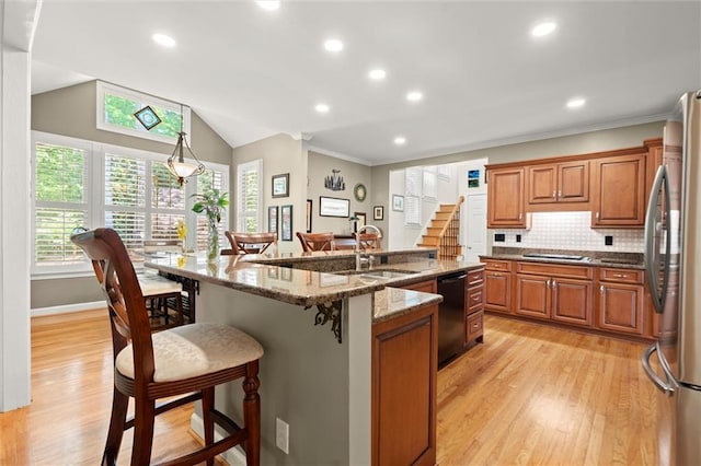 kitchen featuring a kitchen breakfast bar, brown cabinets, a sink, freestanding refrigerator, and black dishwasher