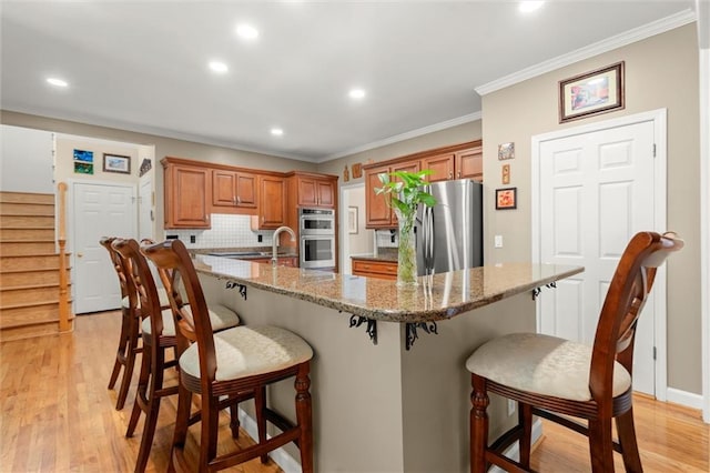 kitchen featuring appliances with stainless steel finishes, brown cabinets, a breakfast bar, recessed lighting, and light wood-style flooring