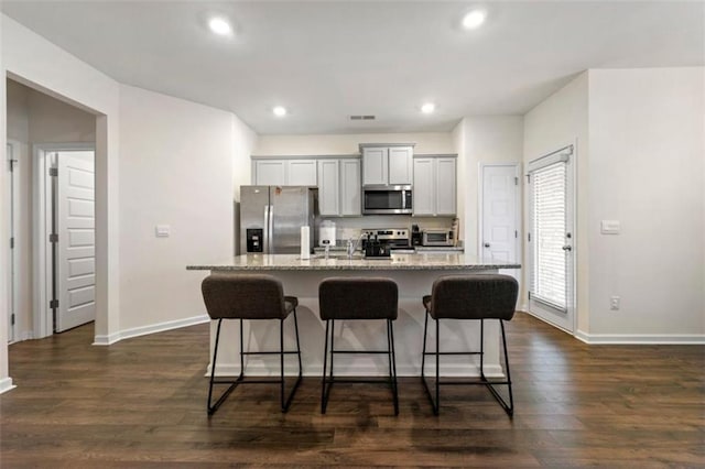 kitchen with visible vents, an island with sink, dark wood-style floors, light stone countertops, and stainless steel appliances