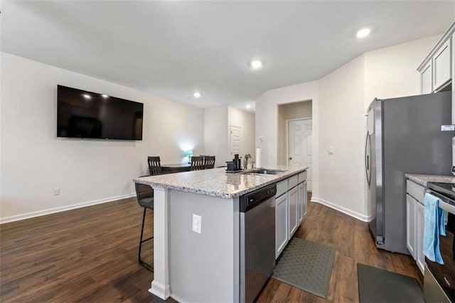 kitchen featuring a center island with sink, light stone counters, a breakfast bar, dark wood-style flooring, and stainless steel appliances