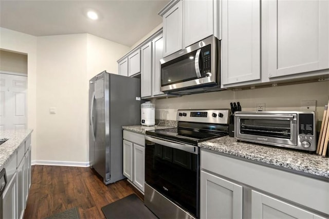 kitchen with a toaster, baseboards, dark wood-style floors, appliances with stainless steel finishes, and light stone countertops