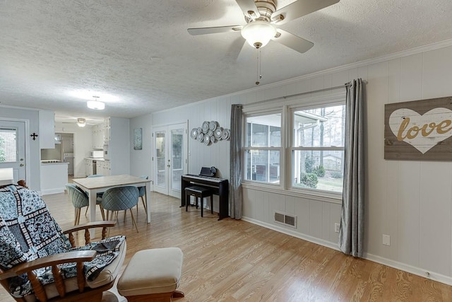 dining room featuring crown molding, ceiling fan, light hardwood / wood-style floors, a textured ceiling, and french doors