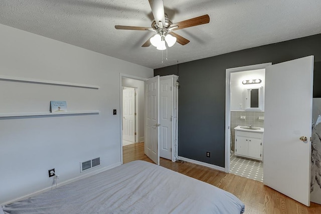 bedroom featuring connected bathroom, sink, light wood-type flooring, ceiling fan, and a textured ceiling