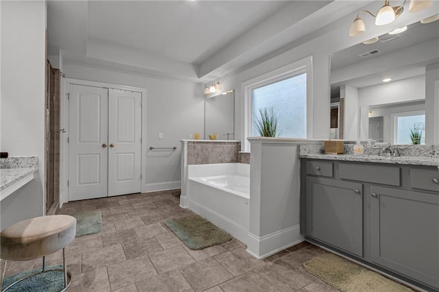 full bath featuring a raised ceiling, a healthy amount of sunlight, vanity, baseboards, and a bath