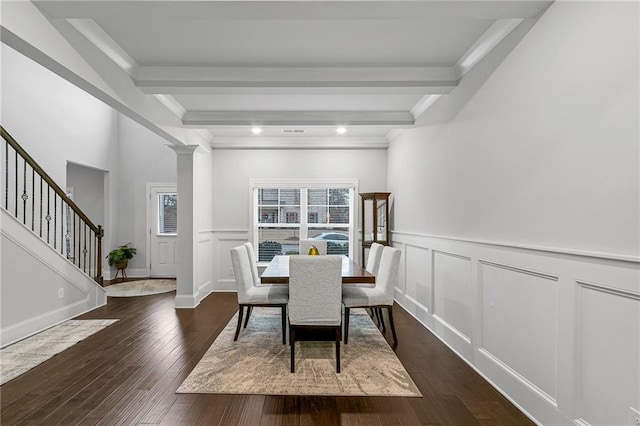 dining room featuring dark wood-style flooring, beam ceiling, a decorative wall, and ornate columns