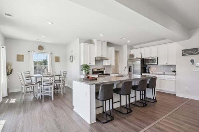 kitchen with white cabinetry, dark hardwood / wood-style flooring, a center island with sink, and appliances with stainless steel finishes