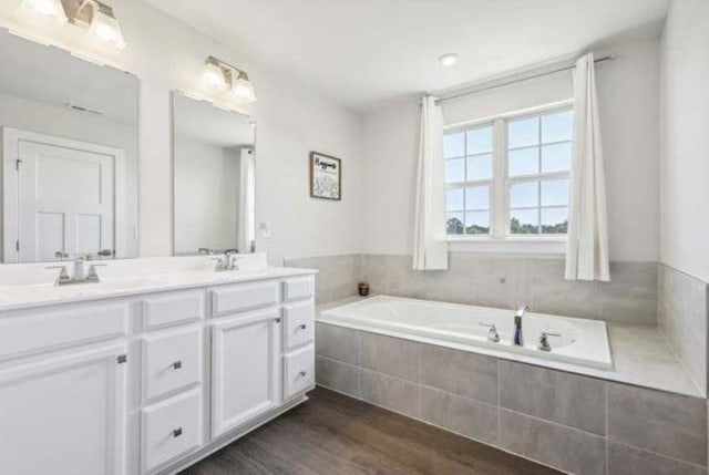 bathroom with a relaxing tiled tub, vanity, and hardwood / wood-style flooring