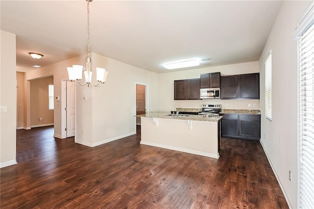 kitchen with a kitchen island with sink, appliances with stainless steel finishes, hanging light fixtures, dark hardwood / wood-style floors, and dark brown cabinetry