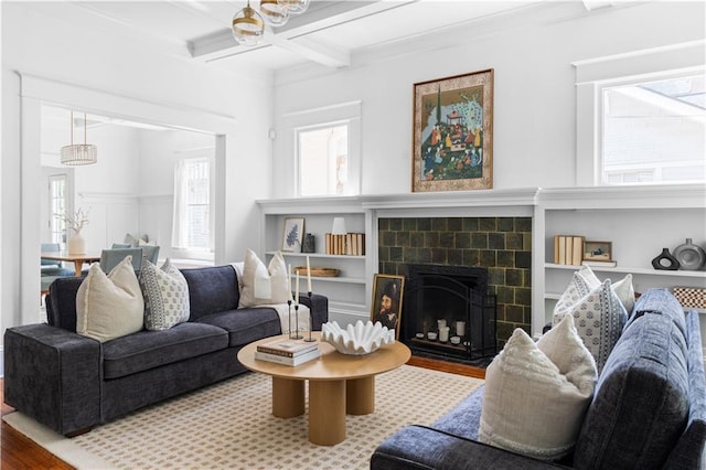 living room with wood finished floors, beamed ceiling, coffered ceiling, a tiled fireplace, and crown molding