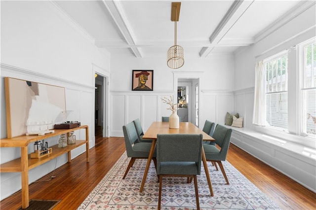 dining area with coffered ceiling, beamed ceiling, a chandelier, wood finished floors, and a decorative wall