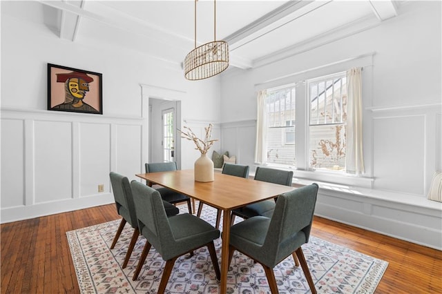 dining area featuring a decorative wall, a chandelier, beamed ceiling, a wainscoted wall, and hardwood / wood-style floors