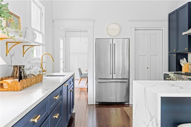 kitchen with high quality fridge, a sink, blue cabinetry, dark wood-type flooring, and light stone countertops