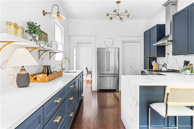 kitchen featuring high end fridge, a sink, blue cabinetry, a peninsula, and dark wood-type flooring