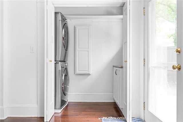 laundry area featuring estacked washer and dryer, dark wood finished floors, cabinet space, and baseboards