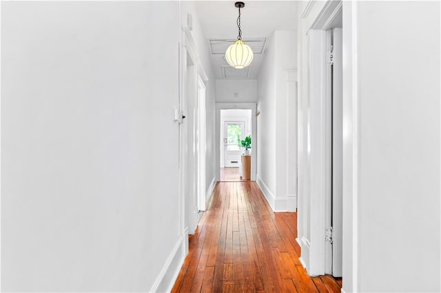 corridor featuring attic access, wood-type flooring, and baseboards