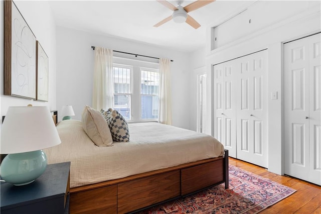 bedroom with wood finished floors, two closets, and ceiling fan