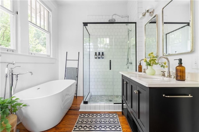 full bath with wood finished floors, a stall shower, double vanity, and a freestanding bath