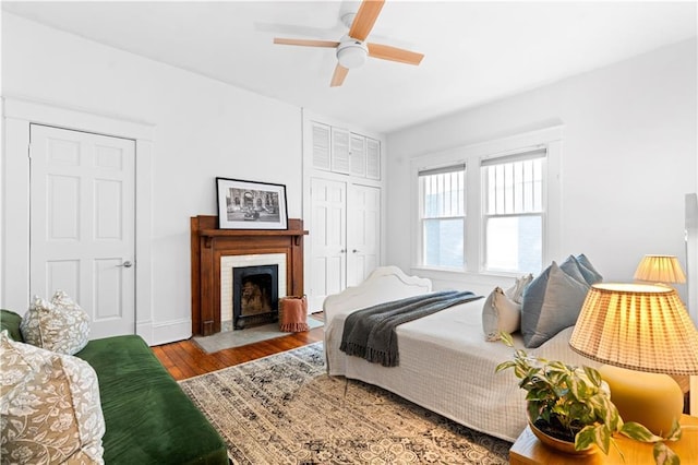bedroom with wood finished floors, a closet, a fireplace with flush hearth, and a ceiling fan