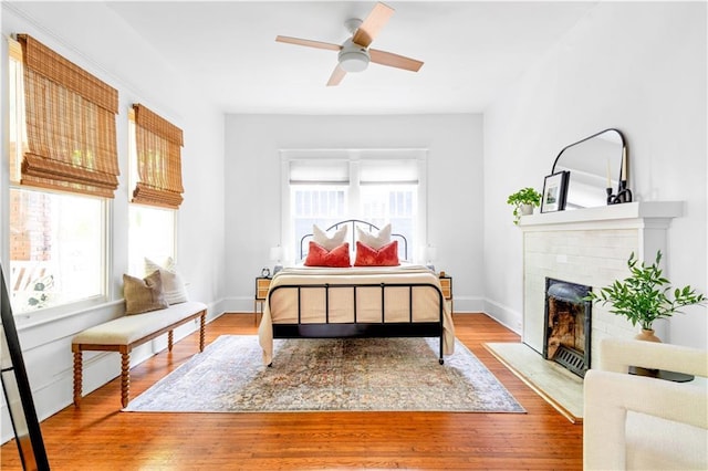 bedroom featuring a fireplace, wood finished floors, ceiling fan, and baseboards