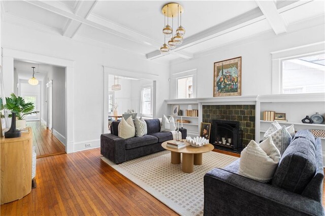 living room featuring coffered ceiling, wood-type flooring, beamed ceiling, baseboards, and a tiled fireplace