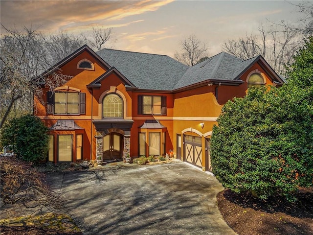 view of front facade with a garage, stone siding, driveway, and stucco siding