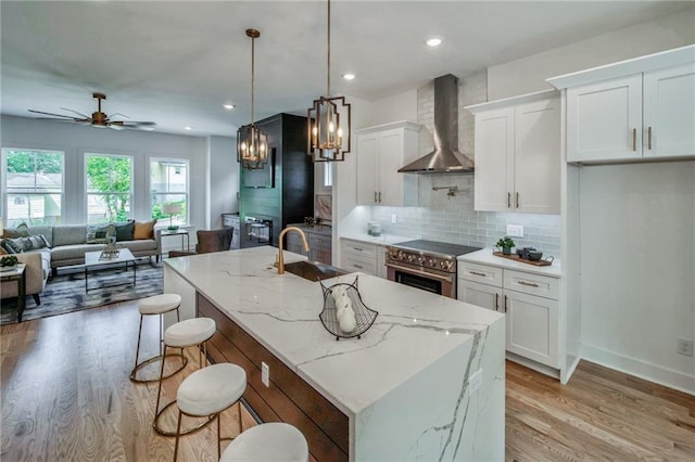 kitchen with white cabinetry, a kitchen island with sink, pendant lighting, wall chimney exhaust hood, and sink