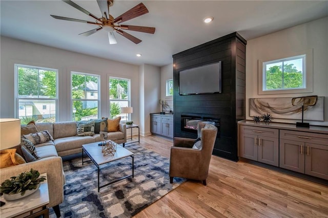 living room with a large fireplace, light wood-type flooring, and ceiling fan