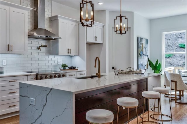 kitchen featuring wall chimney exhaust hood, an island with sink, sink, a breakfast bar, and white cabinetry