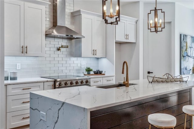 kitchen featuring decorative backsplash, white cabinets, pendant lighting, wall chimney exhaust hood, and light stone counters