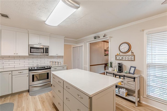 1667 Quail Run, Conyers, GA 30094 - kitchen with appliances with stainless steel finishes, light wood-type flooring, a kitchen island, tasteful backsplash, and a textured ceiling