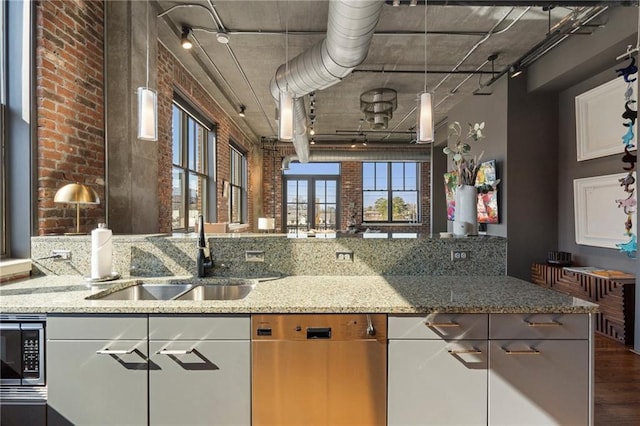 kitchen featuring sink, stainless steel appliances, light stone countertops, white cabinets, and brick wall